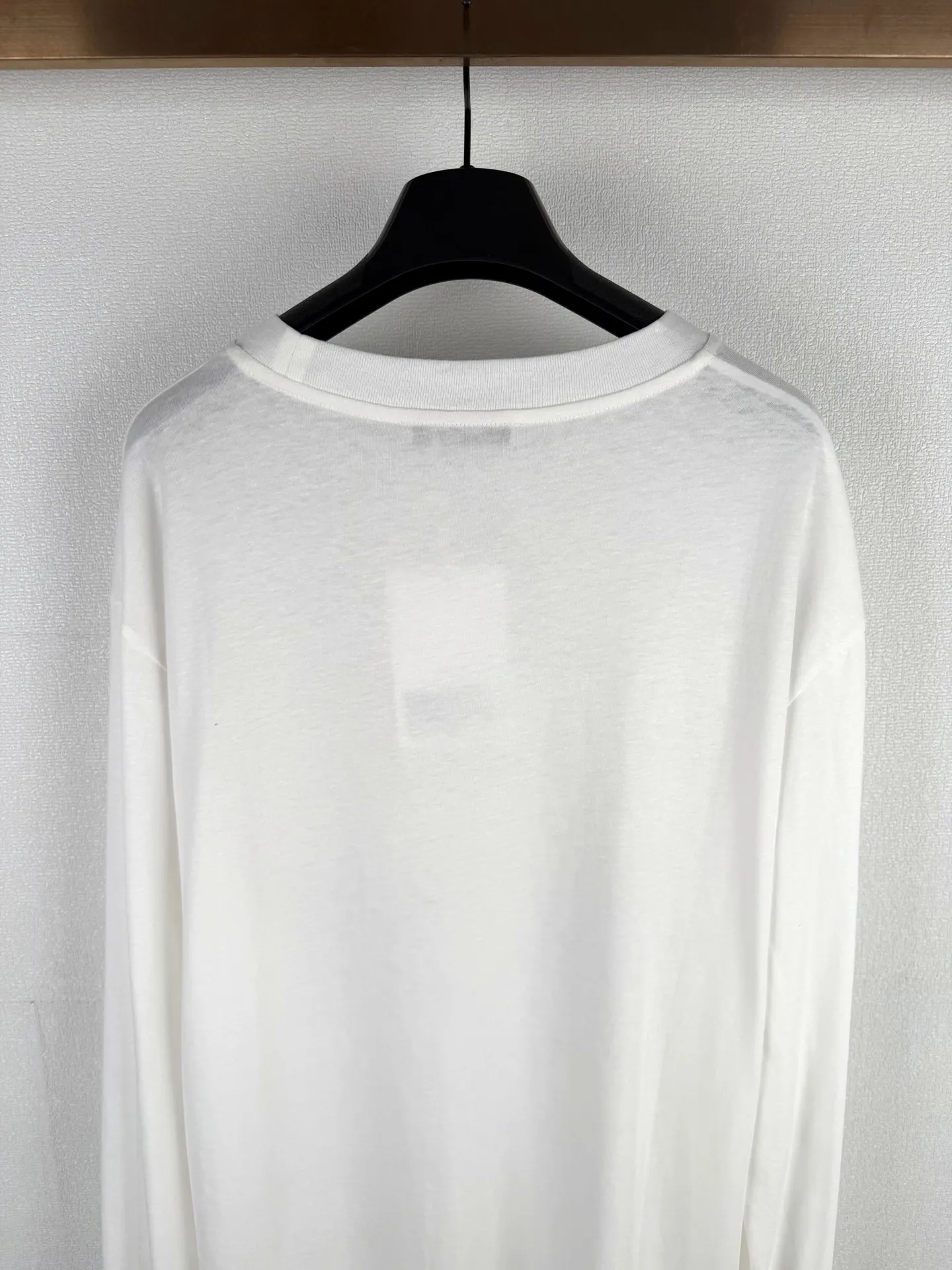 ACNE STUDIOS stamp logo printed long-sleeved T-shirt This long-sleeved round neck style is made of cotton/linen blend jersey fabric with an irregular textured surface for a retro style. Ac stamp logo at front. Relaxed fit, unisex style, hip-length. The fineness of the 32-count yarn ensures a delicate touch, and the introduction of hemp fiber is the finishing touch. It breaks the conventional softness of pure cotton. On the basis of being skin-friendly and soft, it brings natural roughness, knotty particles and micro-wrinkle visual effects, creating an irregular texture of a natural rough base. The fabric is piece-dyed to create a soft, matte finish. Hemp fiber significantly improves moisture wicking properties and provides a dry touch. It has an extremely light and breathable wearing experience. The fabric can naturally drape according to the body contour, forming soft folds, which perfectly serves the casual and loose version, achieving a harmonious unity of material and silhouette. The logo printing on the front is not a simple offset printing, but uses a double-layer process of environmentally friendly elastic glue and varnish. The bottom layer is environmentally friendly elastic glue, which is composed of water-based environmentally friendly resin. After being scraped through screen printing and cured at high temperature, a soft and continuous adhesive film with strong stretch elasticity is formed. This layer of film can perfectly stretch and retract with the fabric, completely solving the problems of cracking and stiffness in traditional printing, and ensuring that the wear on light and thin fabrics does not feel tight. A transparent varnish that is accurately overprinted on the surface creates a high-gloss gloss effect in specific areas, contrasting with the matte or semi-matte texture of the glue. This layer of varnish not only significantly improves the color contrast and three-dimensional layering of the pattern, but also strengthens the wear-resistant and wash-resistant properties, making the printing on the rough hemp base appear elastic, durable and glossy.